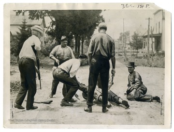 Text on the back reads, "This unusual photo was taken one minute after the shooting of two of the four robbers who were caught in the act of robbing a bank near Morgantown, W. Va. Dr. Defor, seen on the left of the photo, is head of the Vigilance Committee and shot and killed the man on the ground, wounding the other (sitting up), the other two robbers being captured later." 