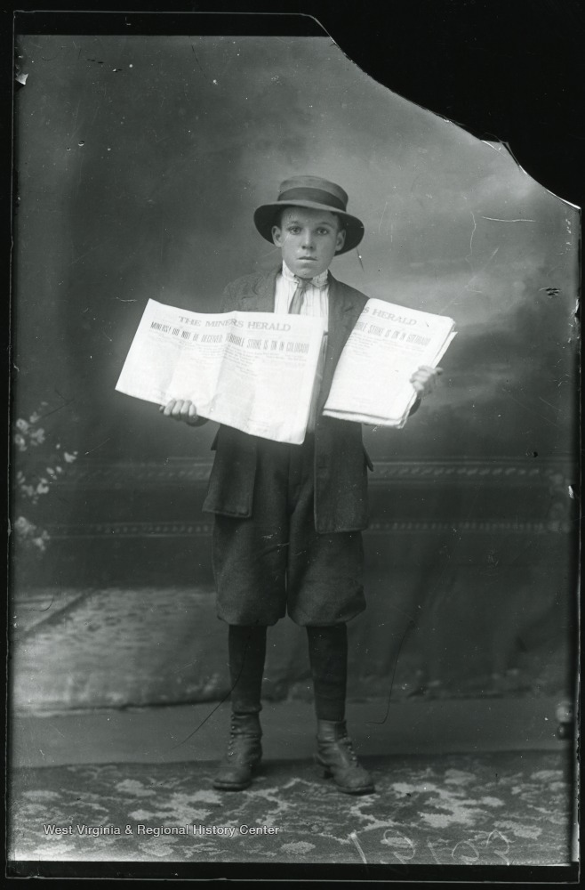 Young boy holding two copies of a The Miner's Herald newspaper, published in Montgomery, W.Va.  The headline reads:  Miners! Do Not be Deceived.  Terrible Strike is on in Colorado.  Copies dated Friday, Oct. 24, 1913.