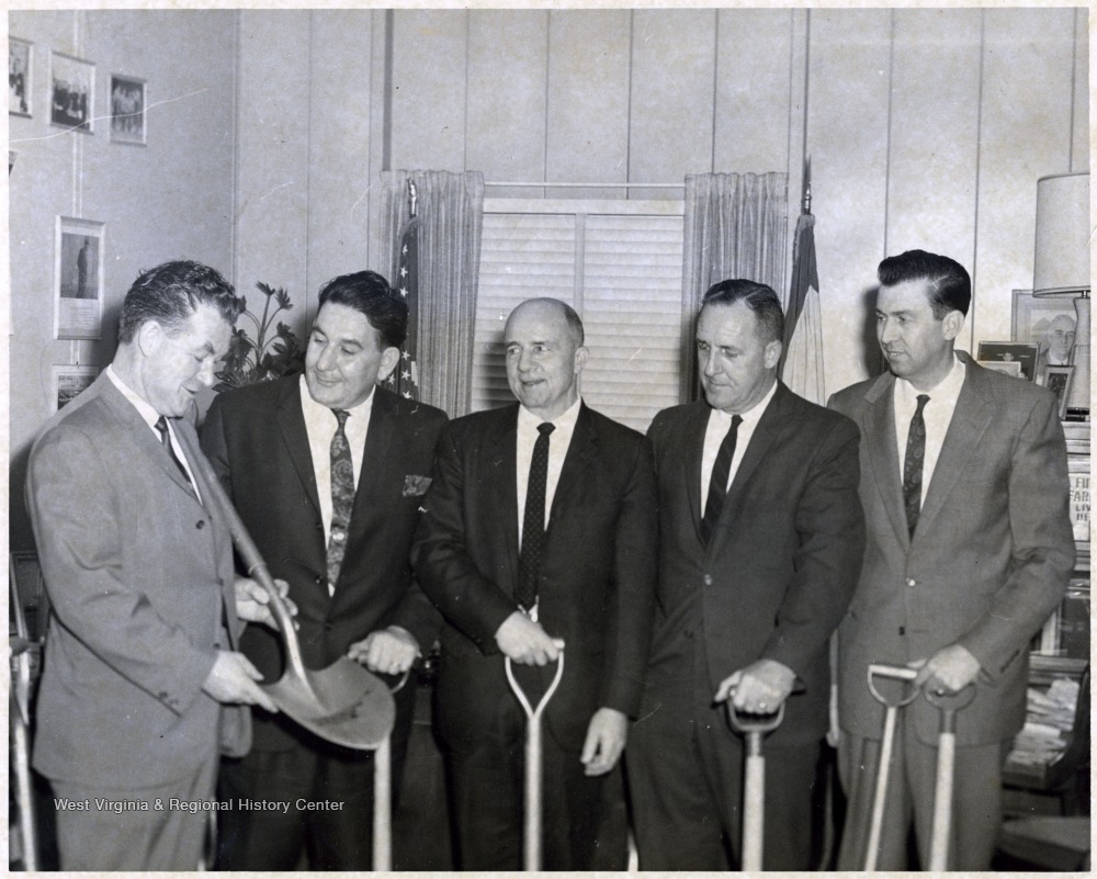 A photograph of A. James Manchin (second from left) holding shovels with others inside an office.