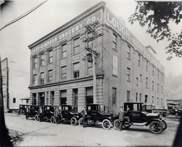 Exterior of Lough-Simpson Grocery Company; employees with company automobiles are in front.<br />
