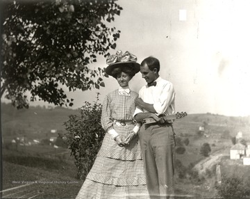 Young couple standing on top of a hill; the woman is wearing a large hat.