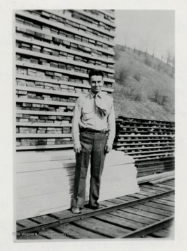 Ray McClelland standing in front of a lumber pile on a train track.  