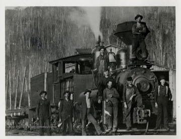 Train engine with crew standing in front and top of it. 