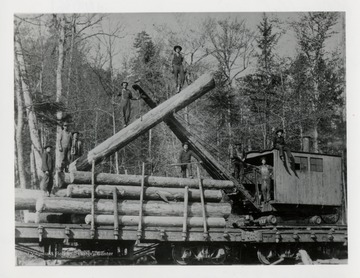Nine men standing on logs and a loader of a railroad car.  