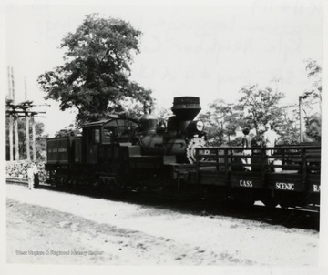Side View of Shay train engine pushing a cart with two men on it.  