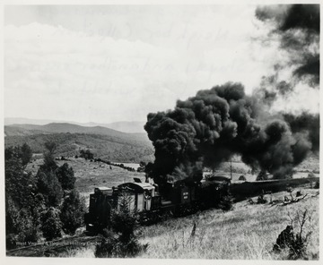 Shay train engine on tracks.  Large smoke cloud coming from smoke stack.  