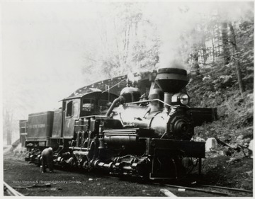 Shay train engine on tracks beside a hill.  