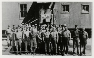 Large group of men standing in front of a building.  Shows E. Mower? standing with men.