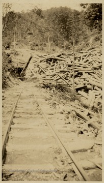 Pile of lumber at the end of train tracks.  Loader visible.