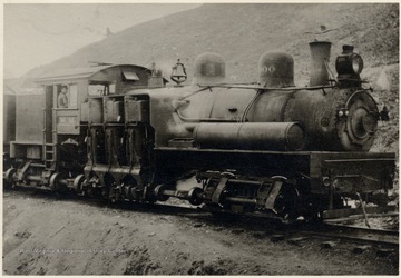 Train engine beside a hillside.  Man in the cabin of the train with W. M. on the Door.