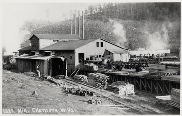 Lumber mill with four smokestacks visible.  Also lumber piles.