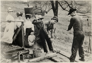 Workers hammering and four women and one child watching.