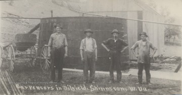 Men pose in front of oil tanks.