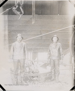 Two men standing beside an oil well.  
