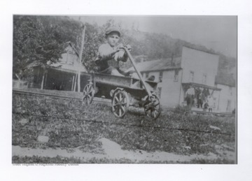 Young boy sitting in a wagon with town buildings behind him.