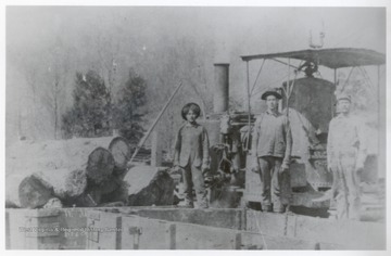 Three loggers stand beside a logging train.