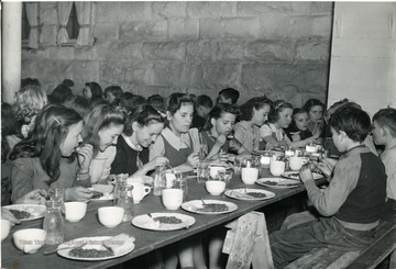 Children in Mason County eating a hot lunch at tables set up on saw horses. 
