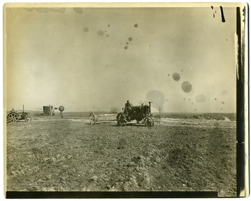 Men spreading lime with tractors on the fields at Arthurdale, getting ready for potatoes.  Small windmill visible in background.