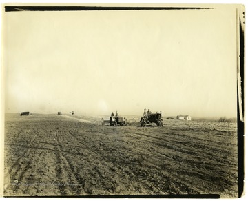 Picture of homesteaders on tractors spreading lime on hilltop land being fitted for potatoes. Note old P.O. truck in background.