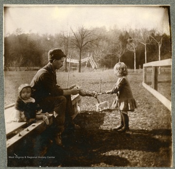 Picture of a man with a baby and a small girl skinning an animal.  Handwritten note on back reads, 'For Minnie and Leone Fron Silas and Oive Sycamore Cottage Sile Philips and Chlidren.'