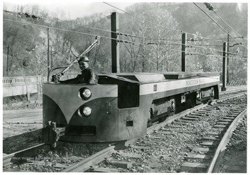Man driving a electric locomotive at the Mathies Mine, W. Va. Copy Print by 'Judge' of good pictures, 954 Liberty Ave. PGH. 22, PA. GR. 1-4288 AT. 1-3834. Reorder Number 29958-17.