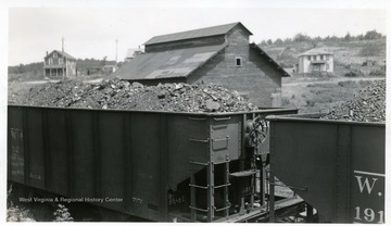 Coal cars with a barn and houses in the background.