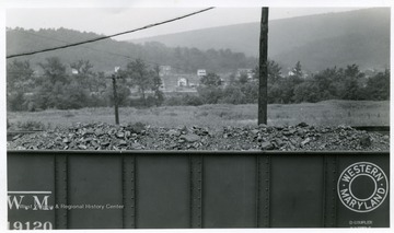 Filled coal car with houses visible in the background.