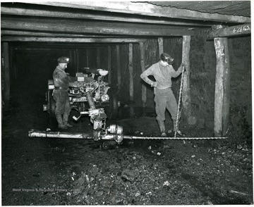 Two men using large bits to drill prior to placing charges.