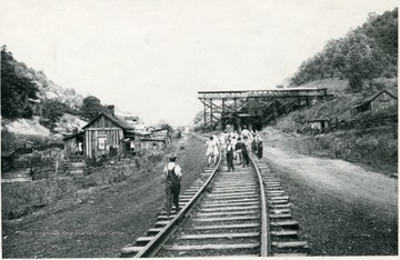 Group walking on railroad tracks with coal buildings all around them. None of the subjects are identified.
