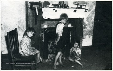Three children of a mining family stand in front of a fireplace.