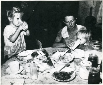 Two children drinking with their mother at the dinner table.