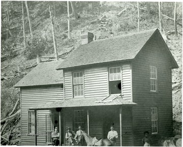 Men on the porch of a house in a coal camp.  Saddled horse standing in front of the porch.