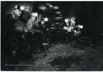 Five miners sitting in mine with their headlamps on.