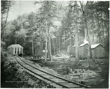 Very early miner's homes, wooden buildings in the woods near train tracks.