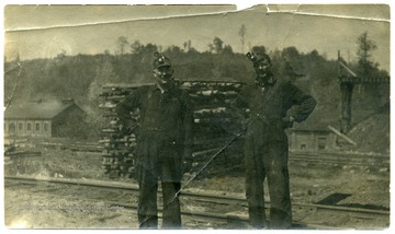 Two miners pose for a picture beside railroad tracks.