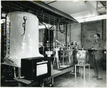 Man standing in a lab with lots of machinery. 'U.S. Bureau of Mines Photo Proof Print.'
