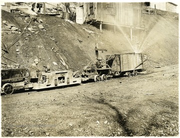 Miner riding on tram with one car spraying something onto the land around the tram. Kanawha County Geological Survey.