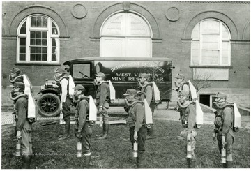 'Students of Mining Engineering at WVU being instructed in mine rescue work.' The students are dressed in rescue attire and the Mine Rescue Car is parked behind them.