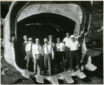 Group of men on tour standing in scoop of large shovel.