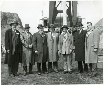Group portrait of men standing in front of large shovel. 