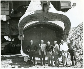 Men stand in front of giant shovel scoop.