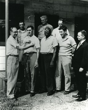 'Company office steps six years of service award. The African American was Harry Wade. Presenter of the award was Charlie Purdere, John Wyatt Receiving award. Rt. of Harry Wade was Floyd Rhodes, next in suit is a Eastern bighsot. Top rt. to lf. Hubert Lawson, Alan Smith, Wylie G. Erwin.'