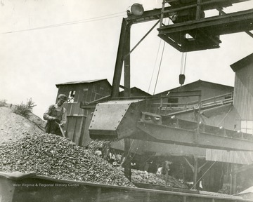 Conveyor outside of preparation plant unloading coal. Miner helps fill up the mine car.
