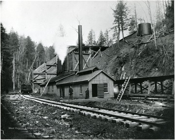 Wooden tipple between tracks and hillside.  Two men stand outside building.