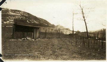 Old shed in the foreground with barracks and a house in the background.