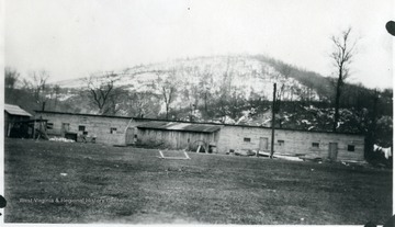 Barracks at Wyatt, W. Va. with piles of lumber stacked and snow covered hillside with laundry hanging on right.