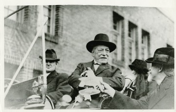 Samuel Gompers, while riding in a car, shaking hands with an unidentified man.