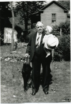 Man holding grandson in one arm and an umbrella in the other. 'Grandson William (Bill) Bennett." 