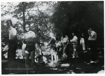 People in bathing suits and others stand in the shade.