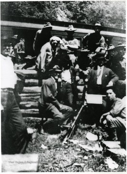 A group of miners is sitting and standing next to a train.